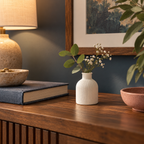 White ribbed gypsum vase with flowers on a walnut console beside a warm lamp.